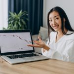 Wanita menunjukkan grafik pasar saham yang menunjukkan tren trafik, menggambarkan pentingnya analisis untuk menghindari kesalahan investasi