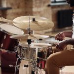 Seorang drummer memainkan drum set dengan fokus, menjaga tempo dan timing di dalam ruangan bergaya industrial
