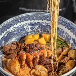 Hidangan mie kari berukuran besar dengan berbagai isian, termasuk udang dan daging