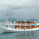 Kapal wisata dua lantai berlayar di perairan Labuan Bajo dengan wisatawan menikmati pemandangan dari dek atas