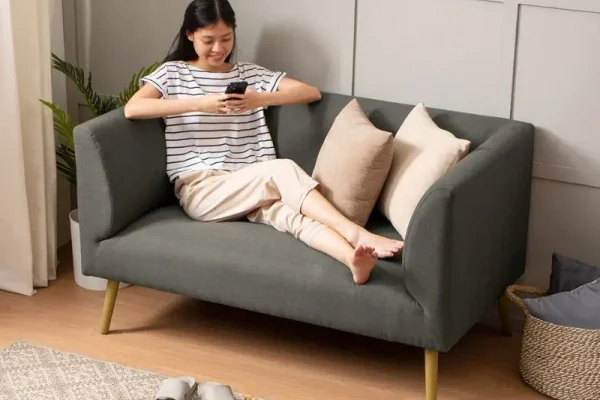 wanita santai duduk di sofa empuk sambil bermain ponsel di ruang tamu minimalis yang nyaman