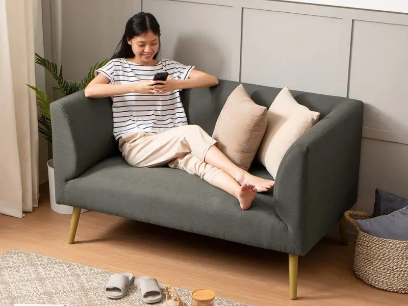 wanita santai duduk di sofa empuk sambil bermain ponsel di ruang tamu minimalis yang nyaman